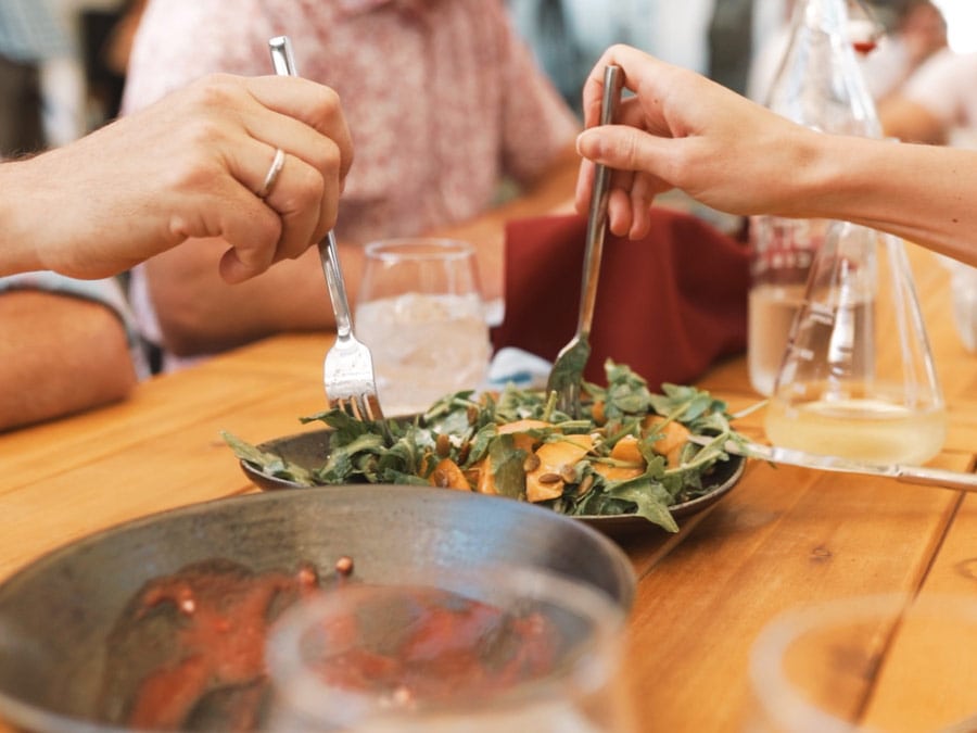 Two people share a salad at a picnic table