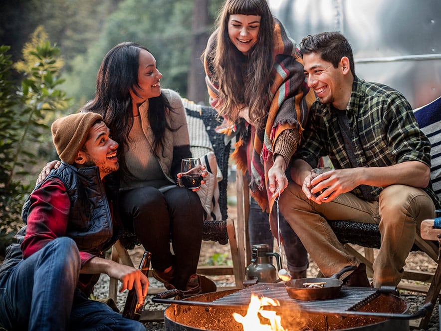 Four friends sit around a campfire roasting marshmallows at AutoCamp, a glamping lodgings made out of Airstreams in Guerneville, Sonoma County, California