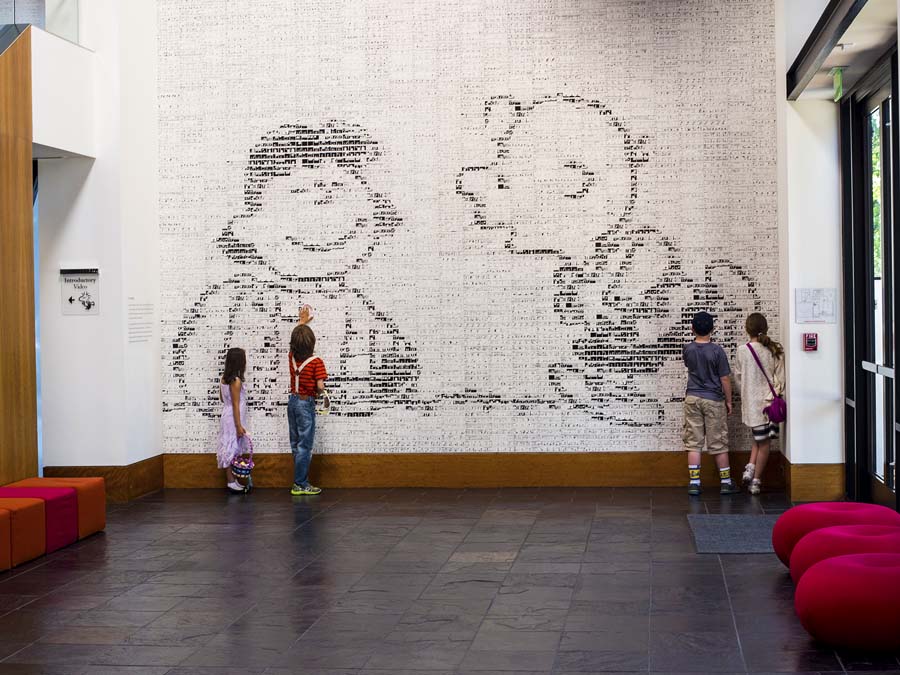 People look at a wall made out of tiny comic strips that forms a large picture