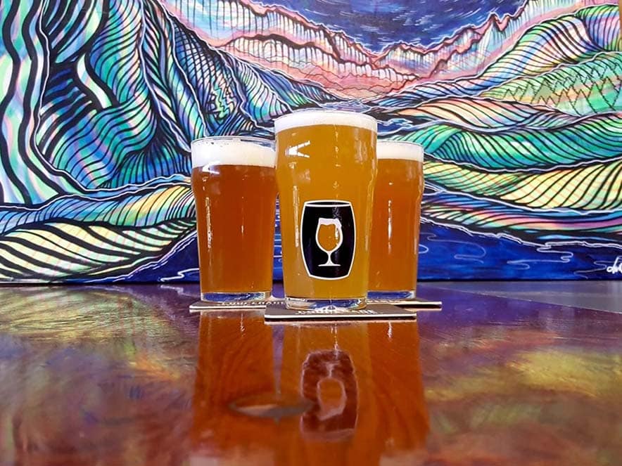 three beer glasses on table with mural in background