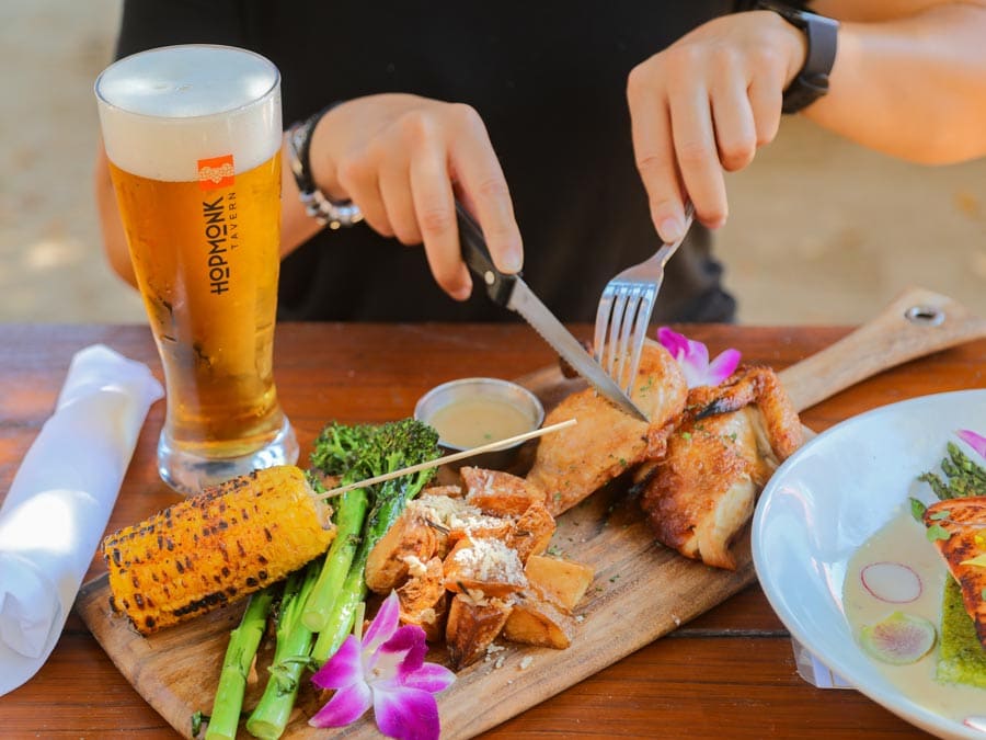 Corn, chicken ,and broccoli are served on a cutting board next to a beer