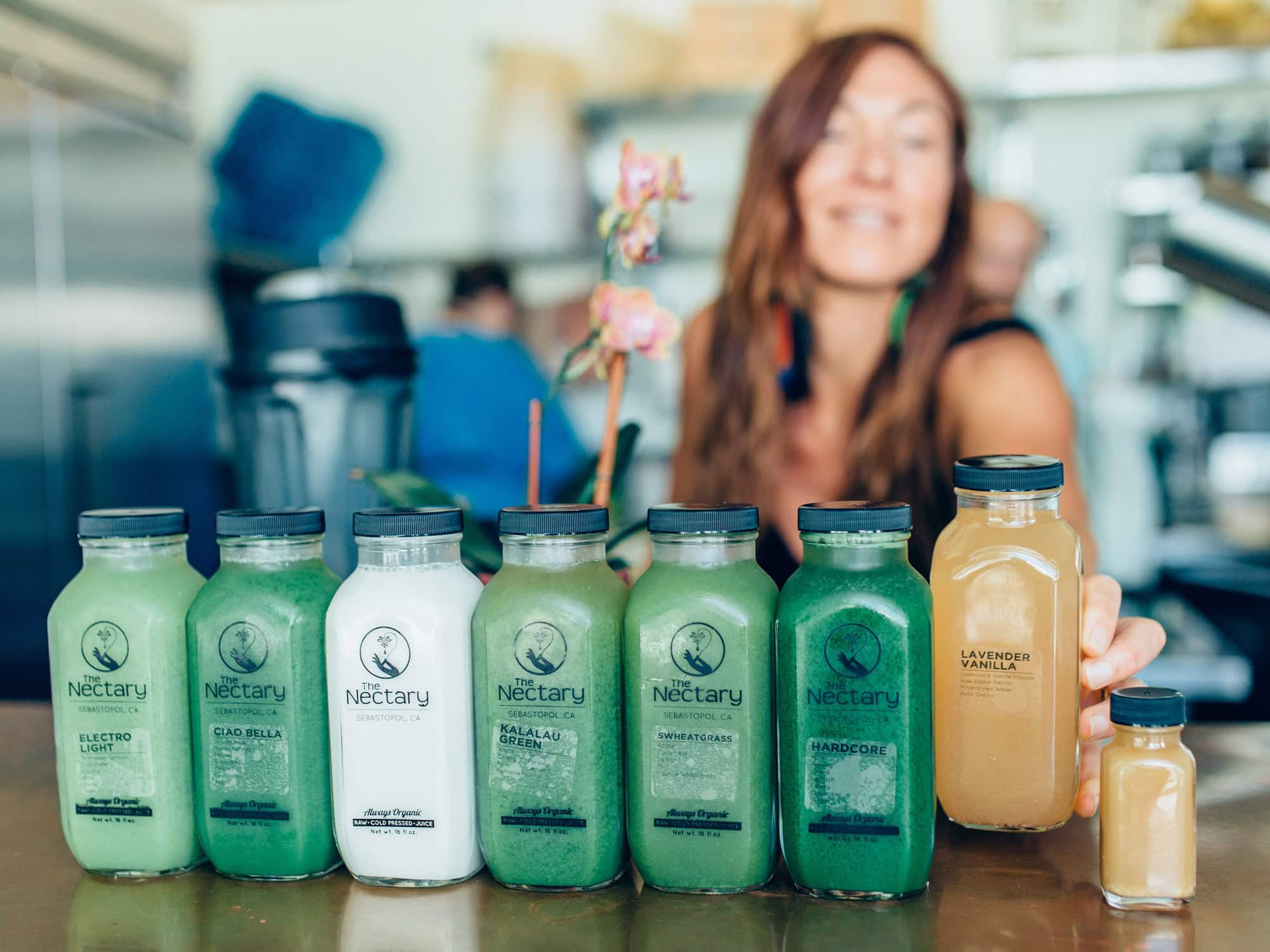 A person smiles while holding bottles of green juic