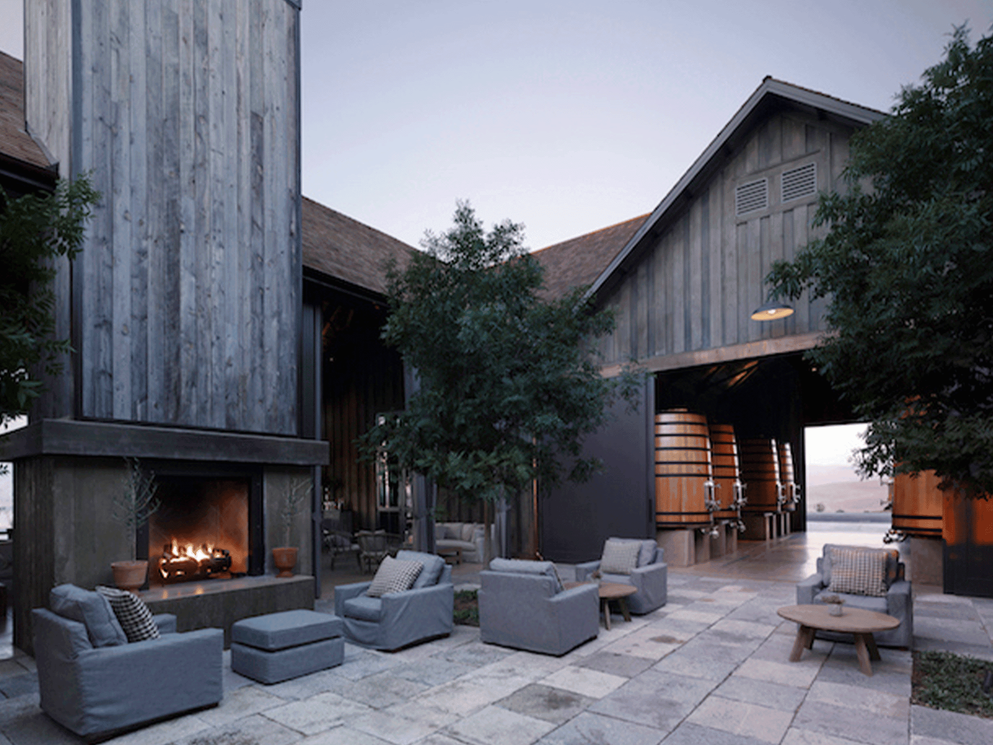 A seated area outside with a fire pit looks in to a storage area for wine tanks