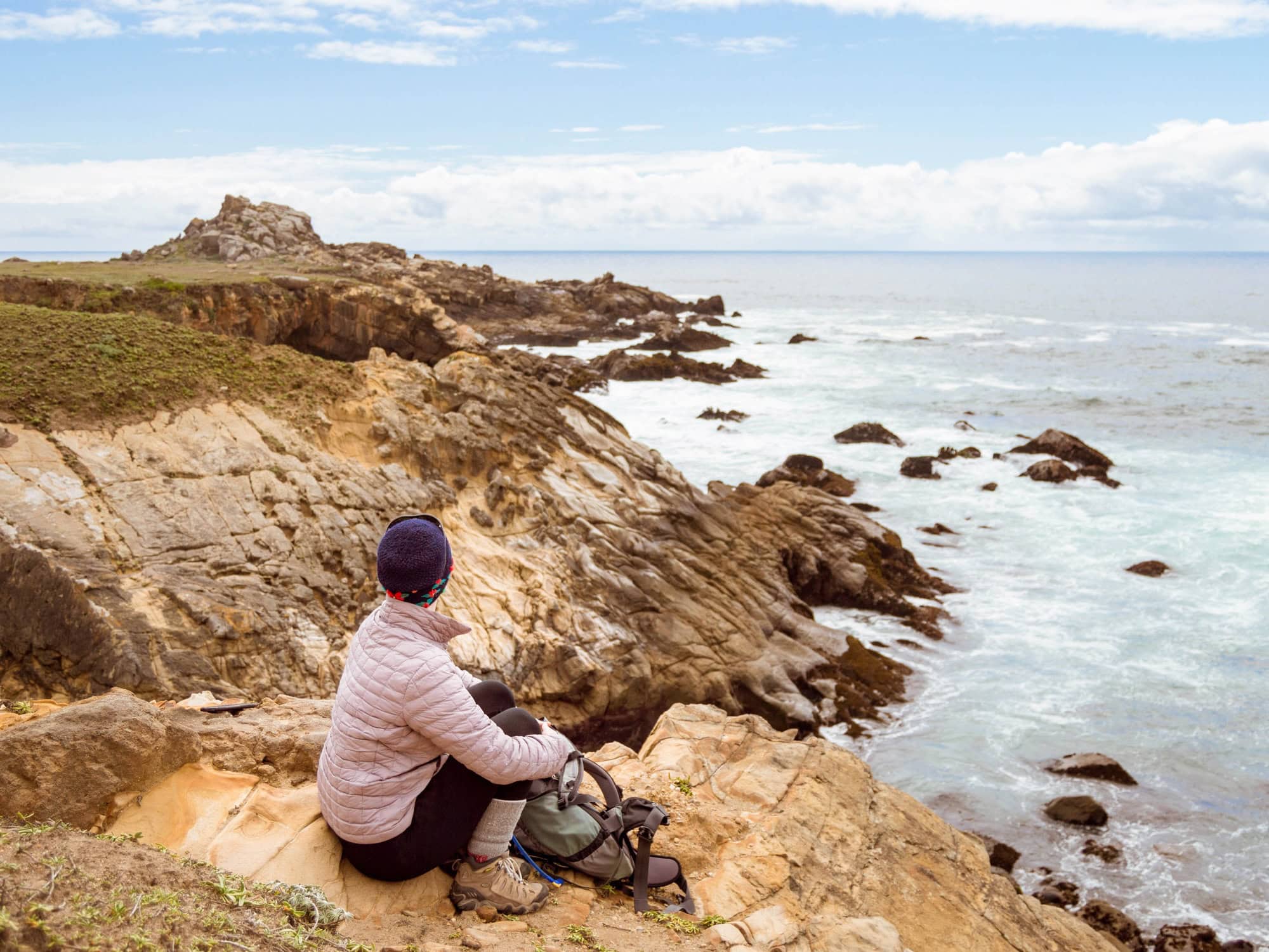 A woman sits on the edge of the coast and looks out over the Pacific Ocean