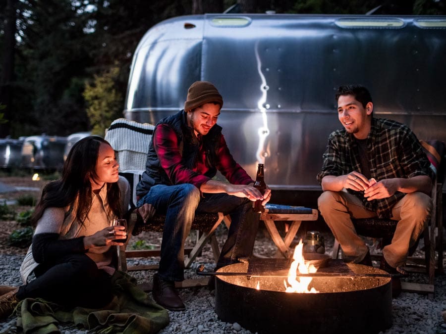 Three people sit around a campfire in front of a luxury Airstream at AutoCamp Russian River in Guerneville