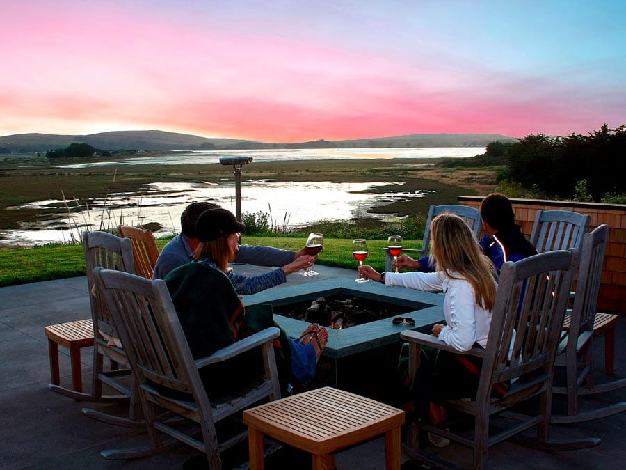 People toast wine glasses by a fire pit overlooking the Pacific Ocean in Sonoma County