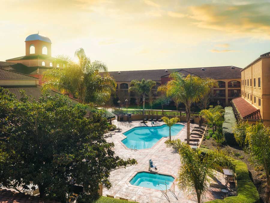 The pool shines in the setting sun and is surrounded by palm trees