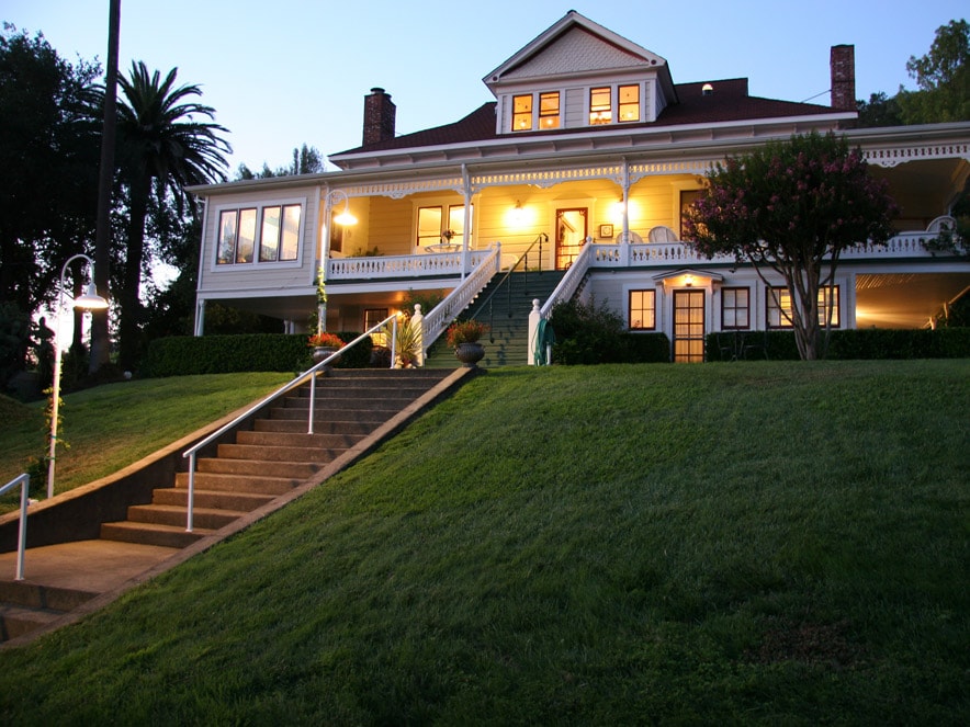 The inn is percehd on a knoll and surrounded by a green lawn and palm trees in Sonoma County