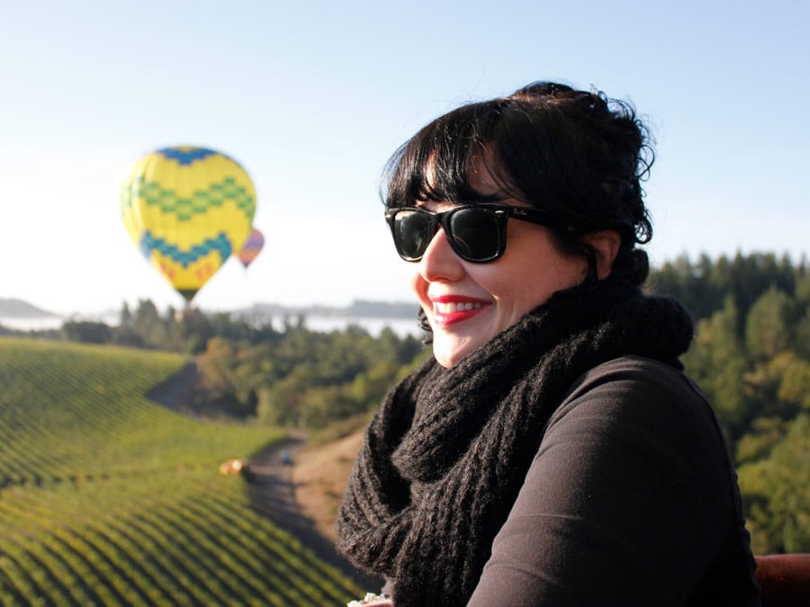 A woman floats above vineyards in a hot air balloon