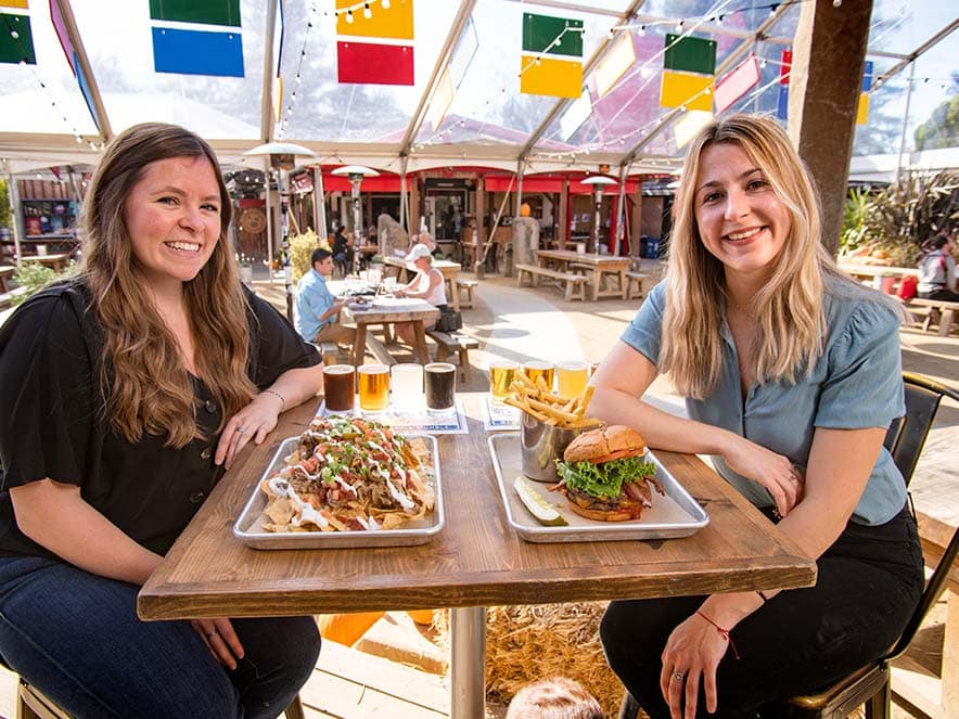 two women at table with food and beer outdoors