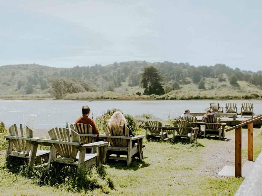 people on picnic tables on grass looking out at ocean