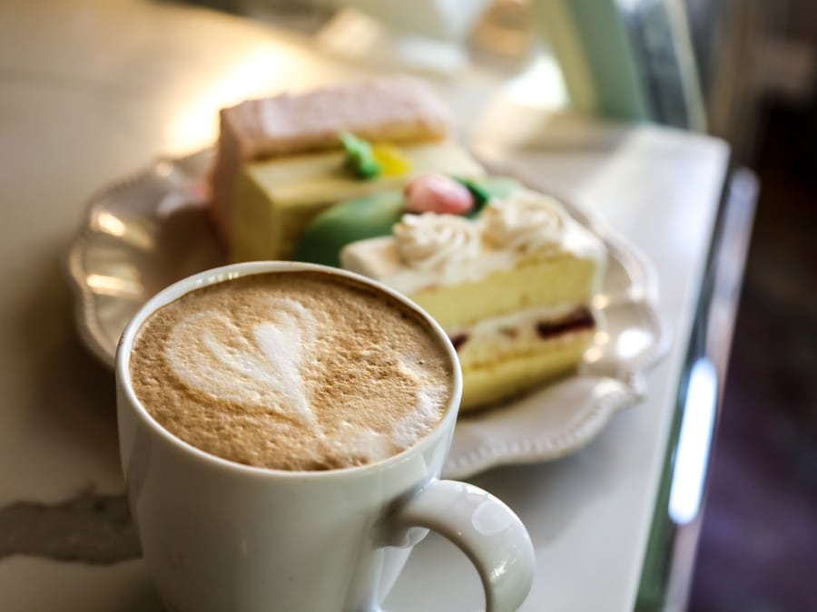 A latte with a heart in the foam and a slice of cake