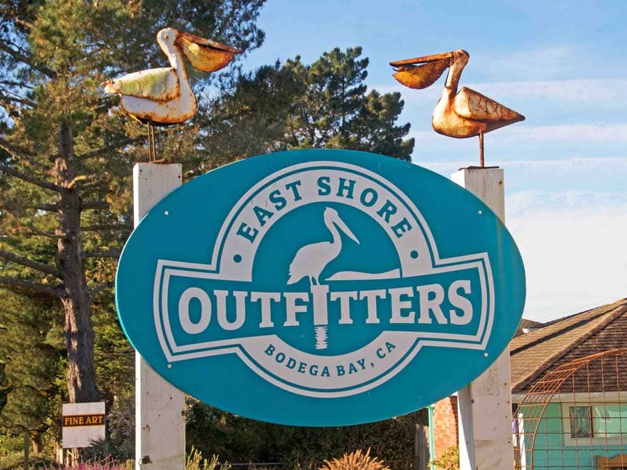 A blue sign for the shop has two metal pelican sculptures sitting on top