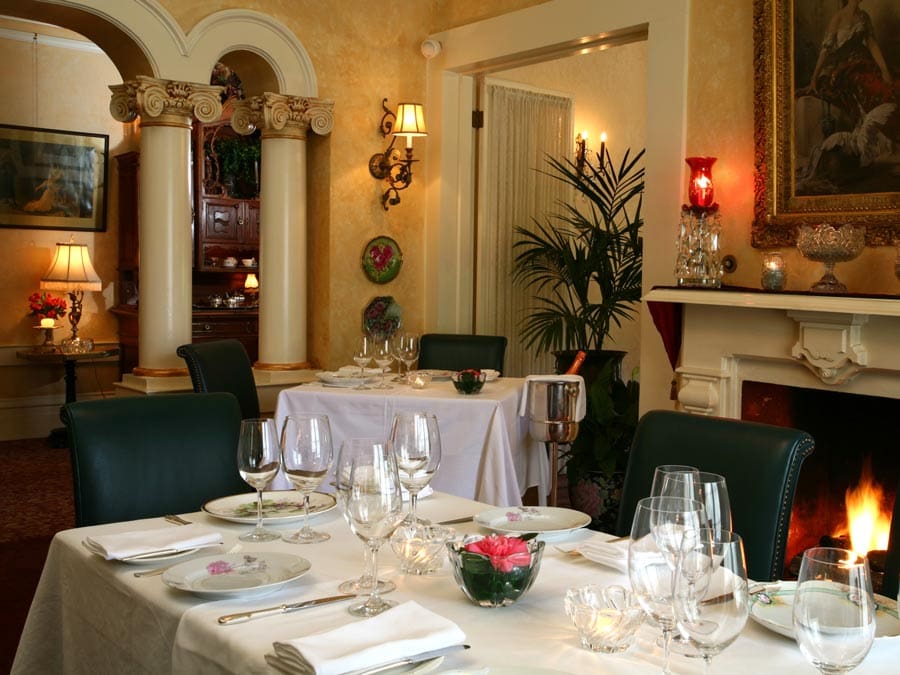 A table is set next to a fireplace in the elegant dining room of Madrona Manor Wine Country Inn & Restaurant in Sonoma County