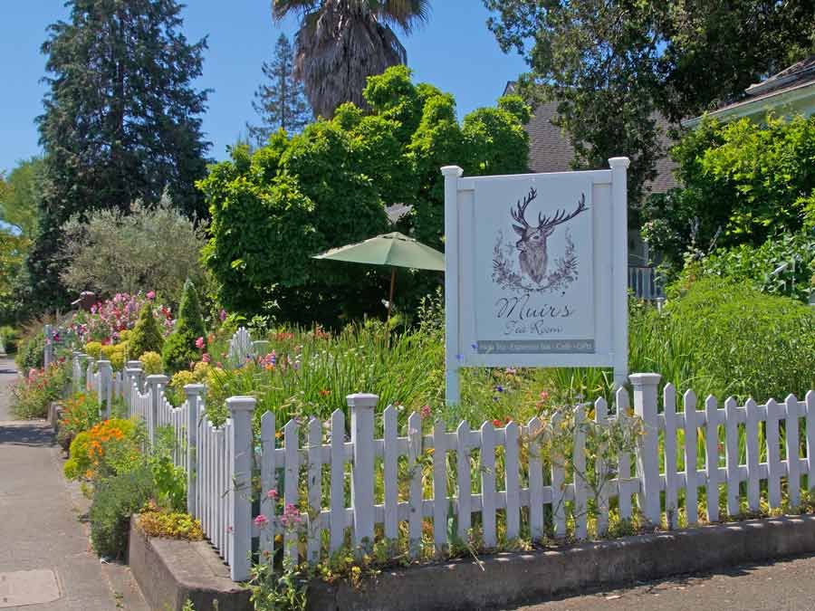 The garden has many blooming flowers and a white picket fence in front of the restaurant