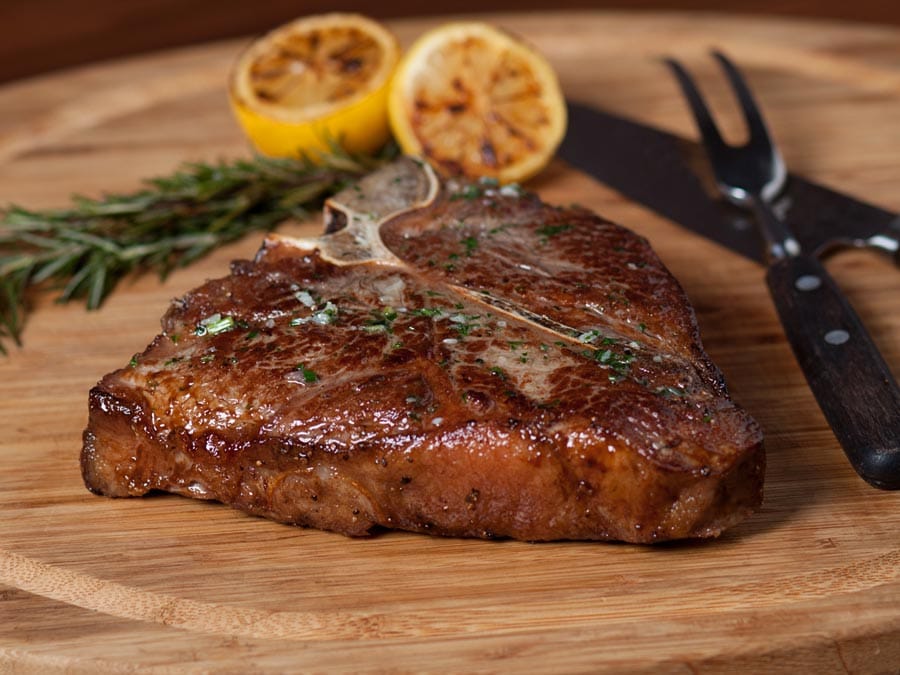 A t bone steak with charred lemons and rosemary on a cutting board