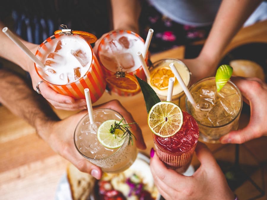 Hands hold colorful cocktails with garnishes of fruit