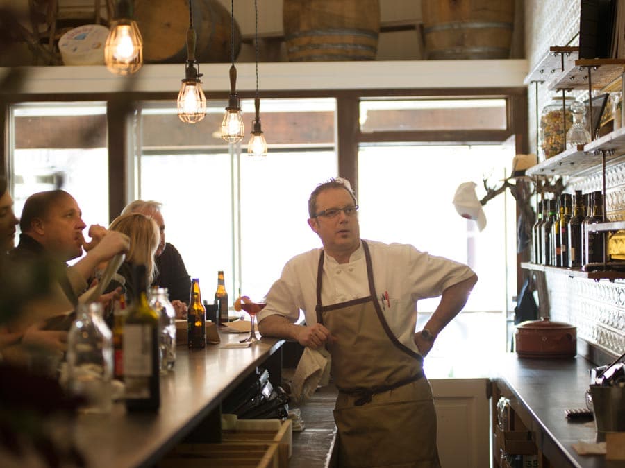 A chef stands behind the bar chatting with patrons