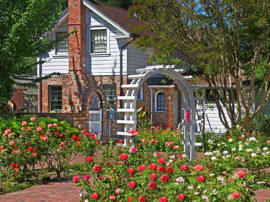 A white arch sits outside of the historic home surrounded by the gardens