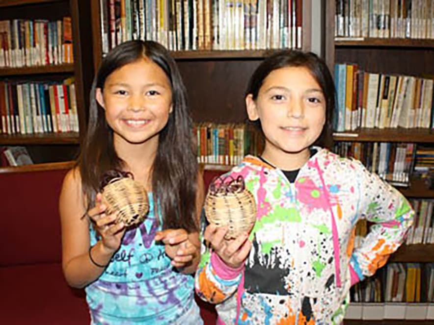 Two indigenous girls hold up baskets at the California Indian Cultural Center