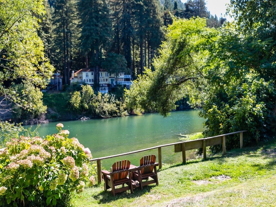 Two wooden chairs on a green lawn beside the light blue Russian River 