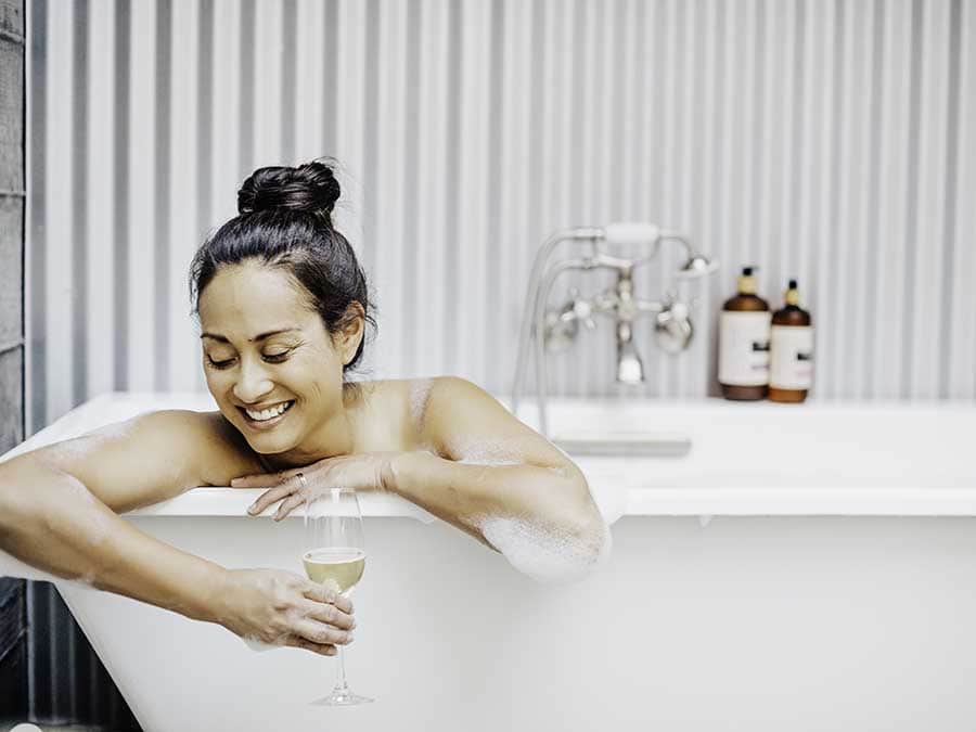 A person sits in a classic bath tub holding a glass of wine