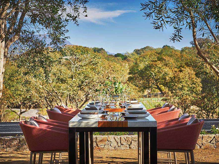 long table set for a meal among trees with views of the hills