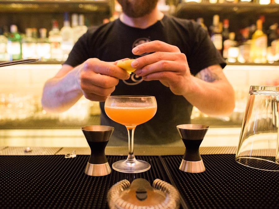 A bartender squeezes a citrus rind into a cocktail