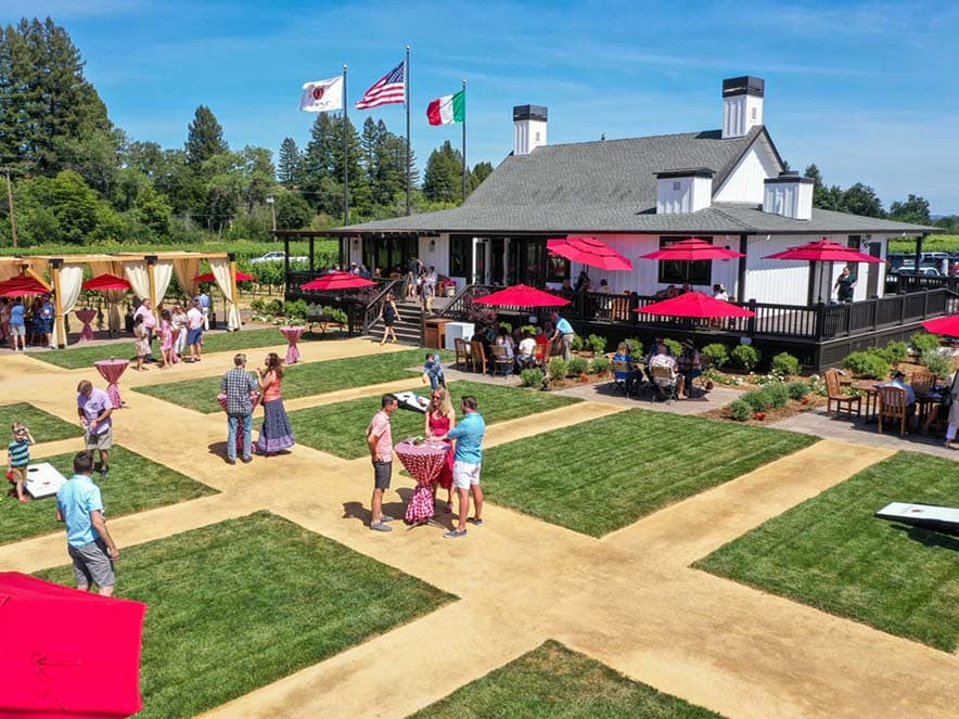 building with red umbrellas and people on the lawn around picnic tables