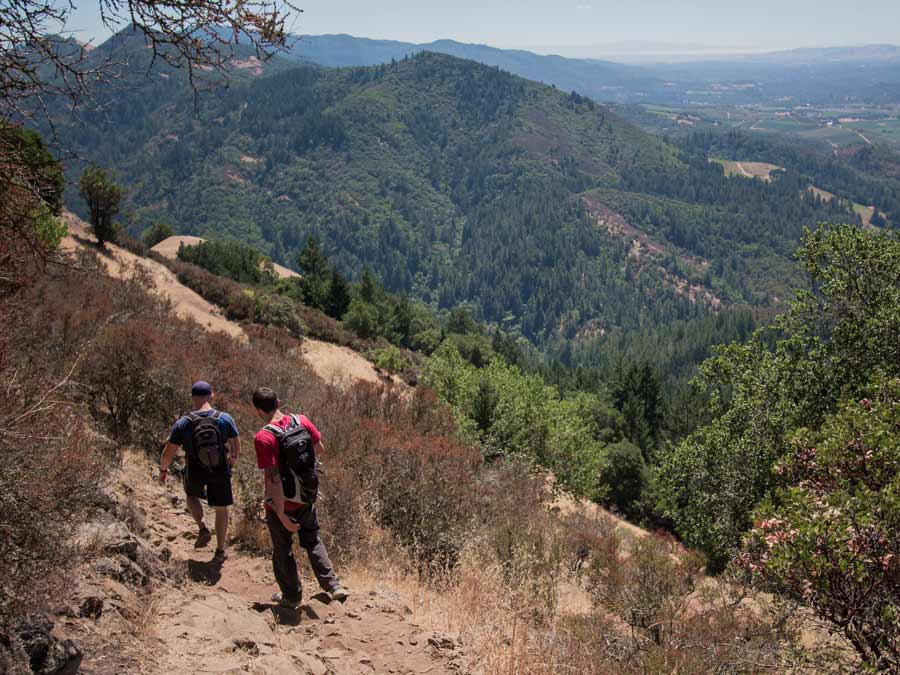 Two people wearing backpacks hike on a rugged trail