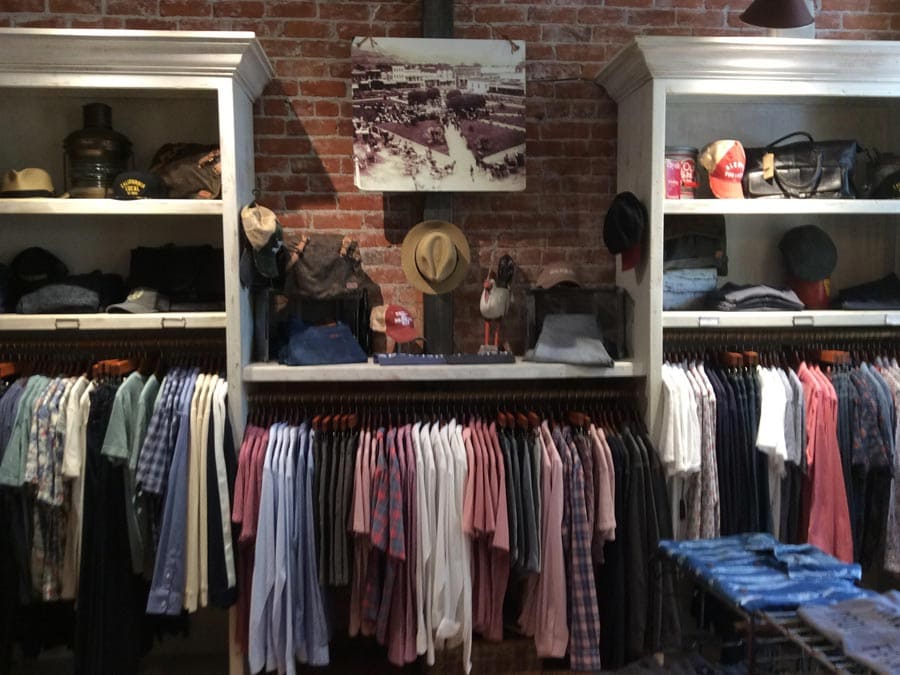 A brick wall has a rack with many men's shirts on display