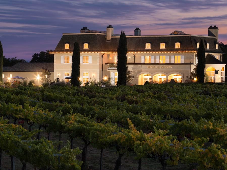 The chateau is lit up at night in front of a colorful sky from the setting sun