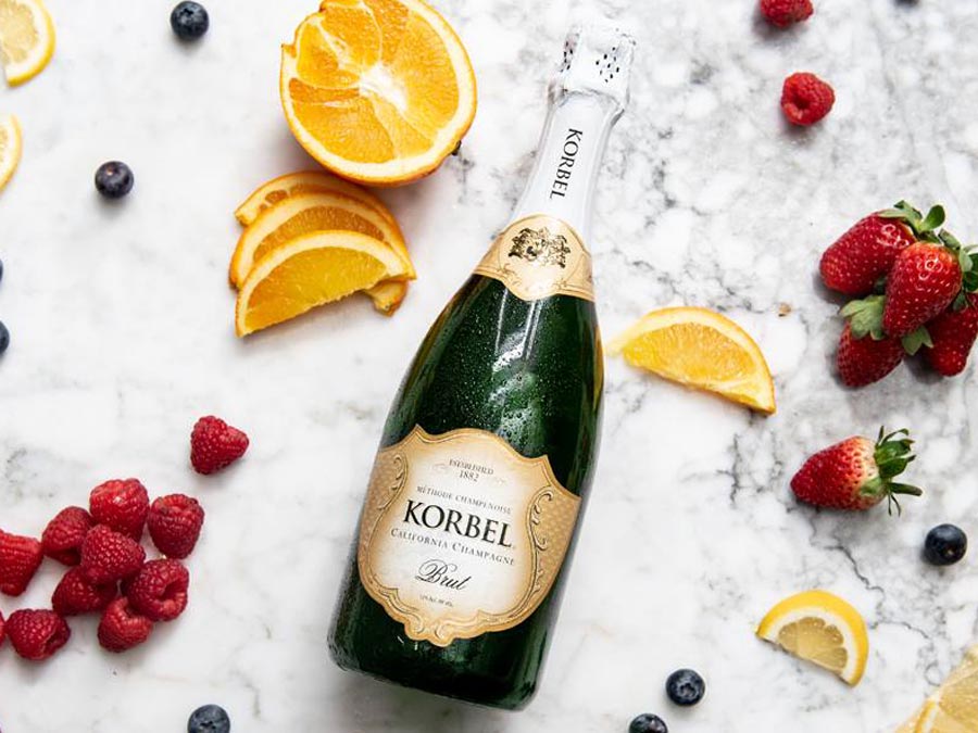 A bottle of Korbel Brut on a marble table surrounded by orange and raspberries