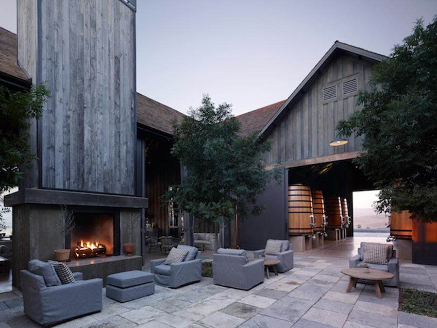 A seated area outside with a fire pit looks in to a storage area for wine tanks