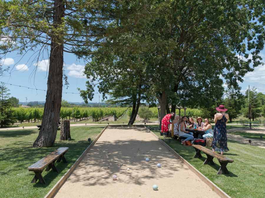 People sit at a pincic table next to a bocce court under a redwood tree in Sonoma County