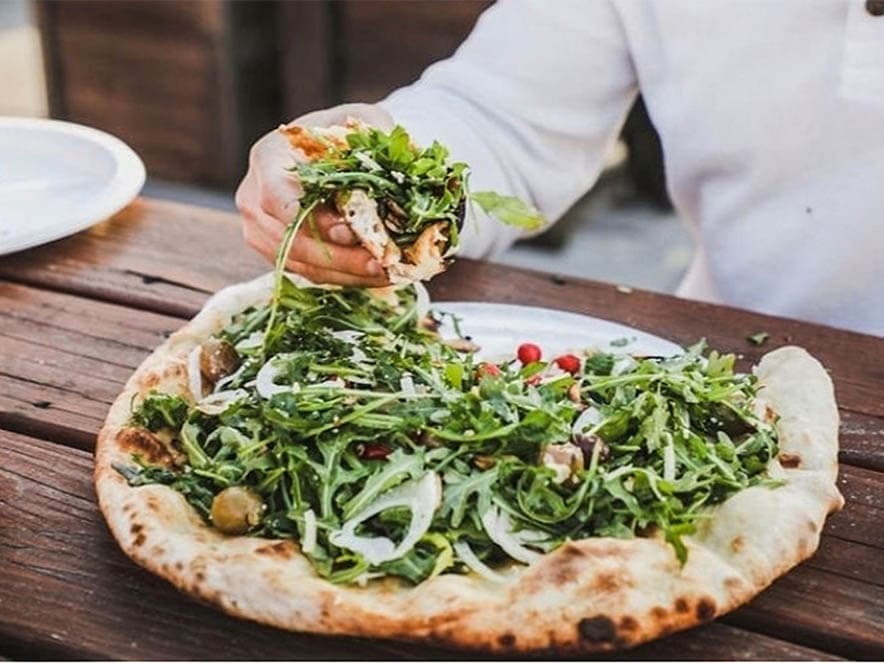 pizza with hand grabbing handful of arugula from the top