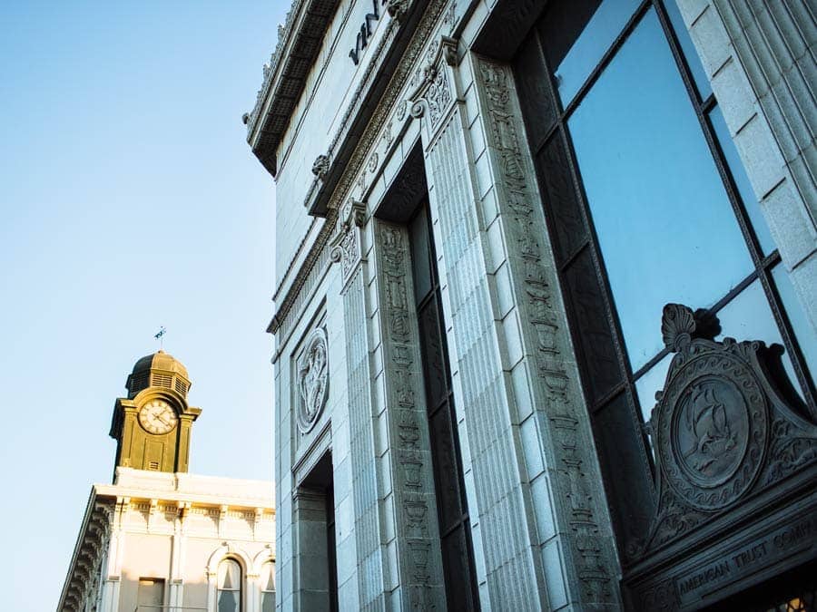 A clock tower is reflected in the windows of a Victorian building