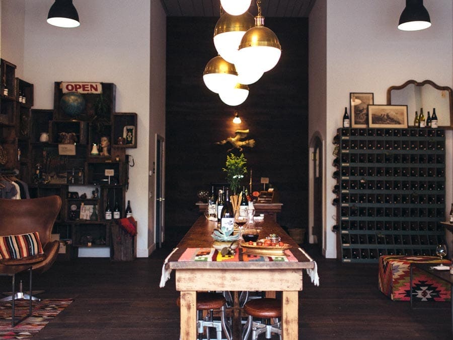 The interior of the tasting room has a wooden table, modern light fixtures, and bohemian style fabrics