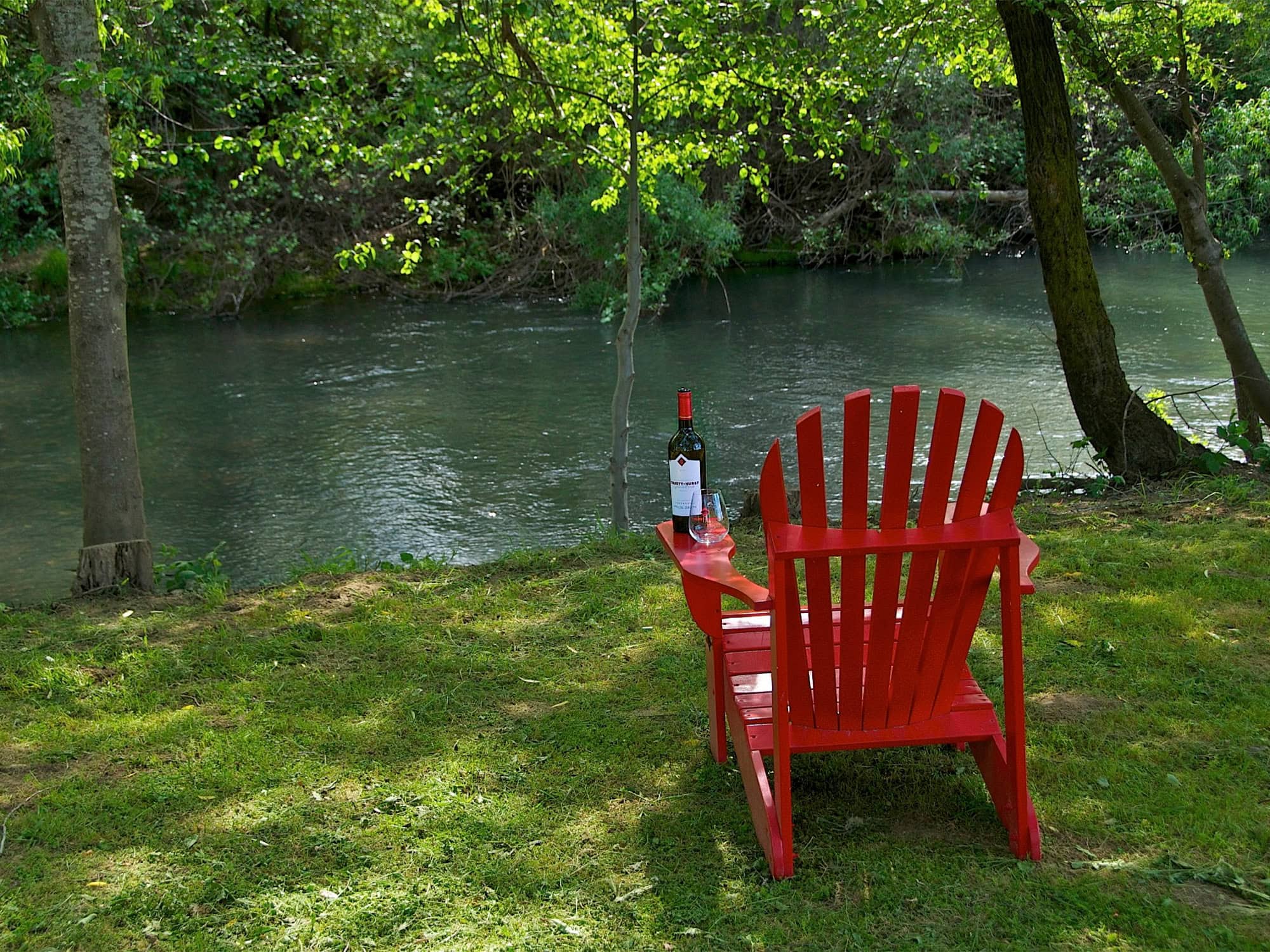 red chair along the river with a bottle of wine at truett hurst winery in healdsburg